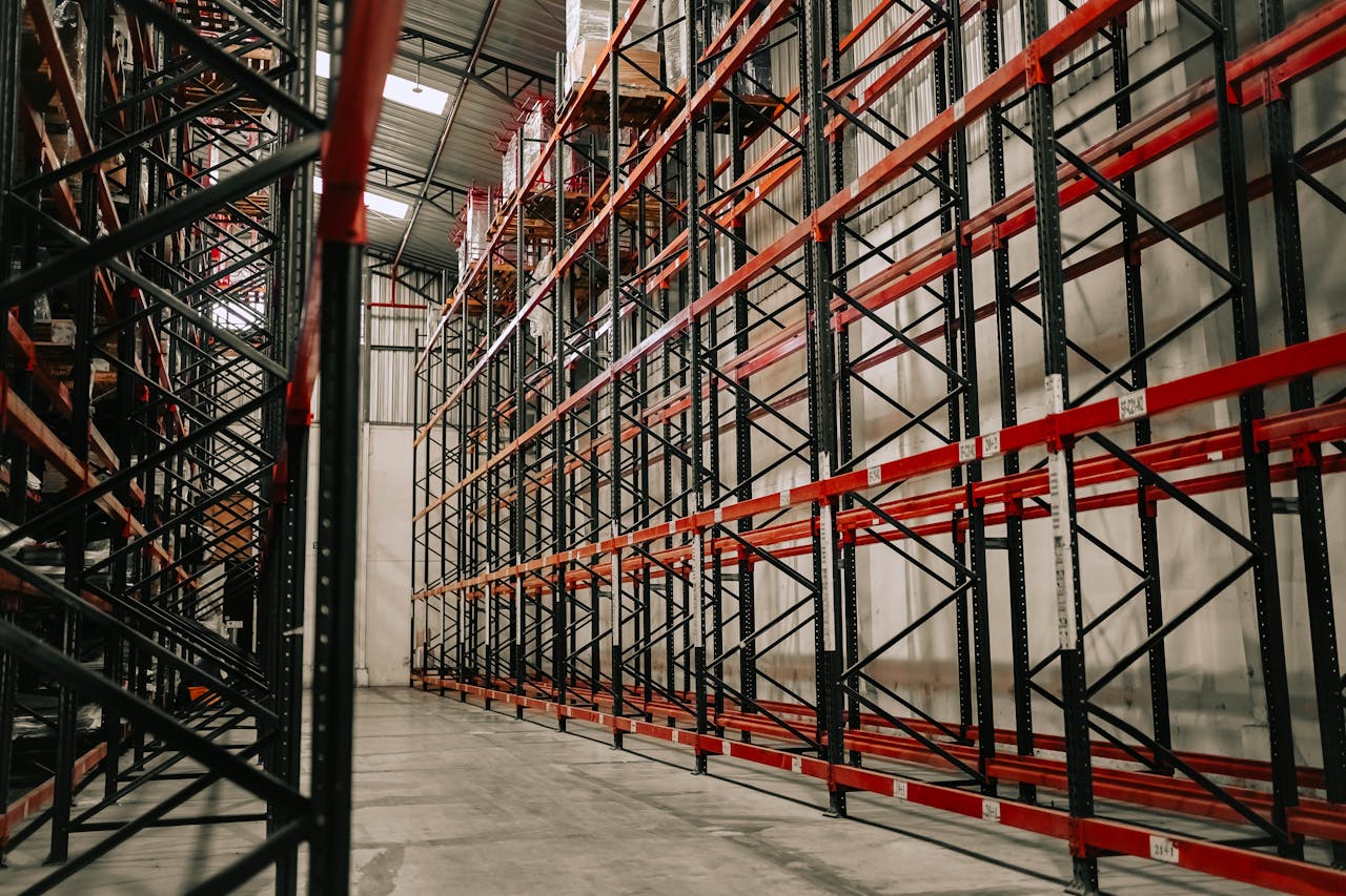services-01 Spacious warehouse interior featuring empty metal racks and high ceiling.
