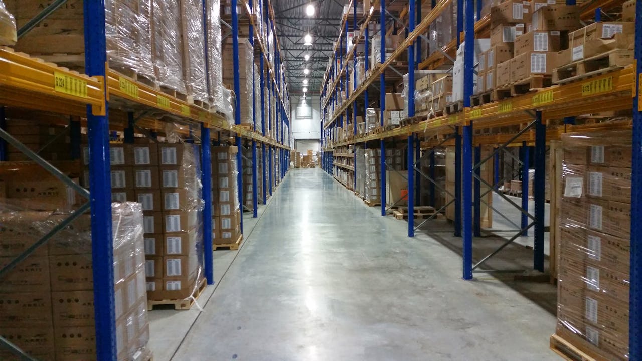 services-02 Interior view of a large warehouse aisle lined with stacks of organized cardboard boxes.